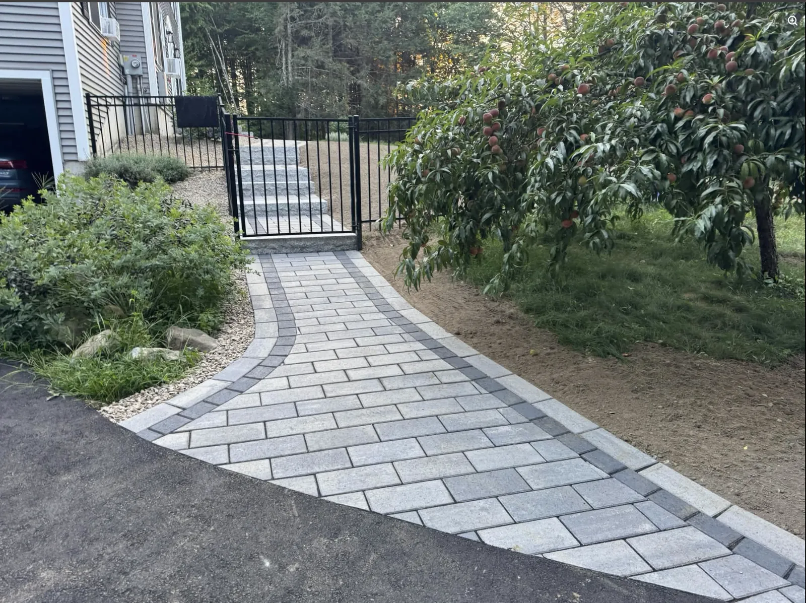 Finished paver walkway leading through a New Hampshire property to stone steps and a gate